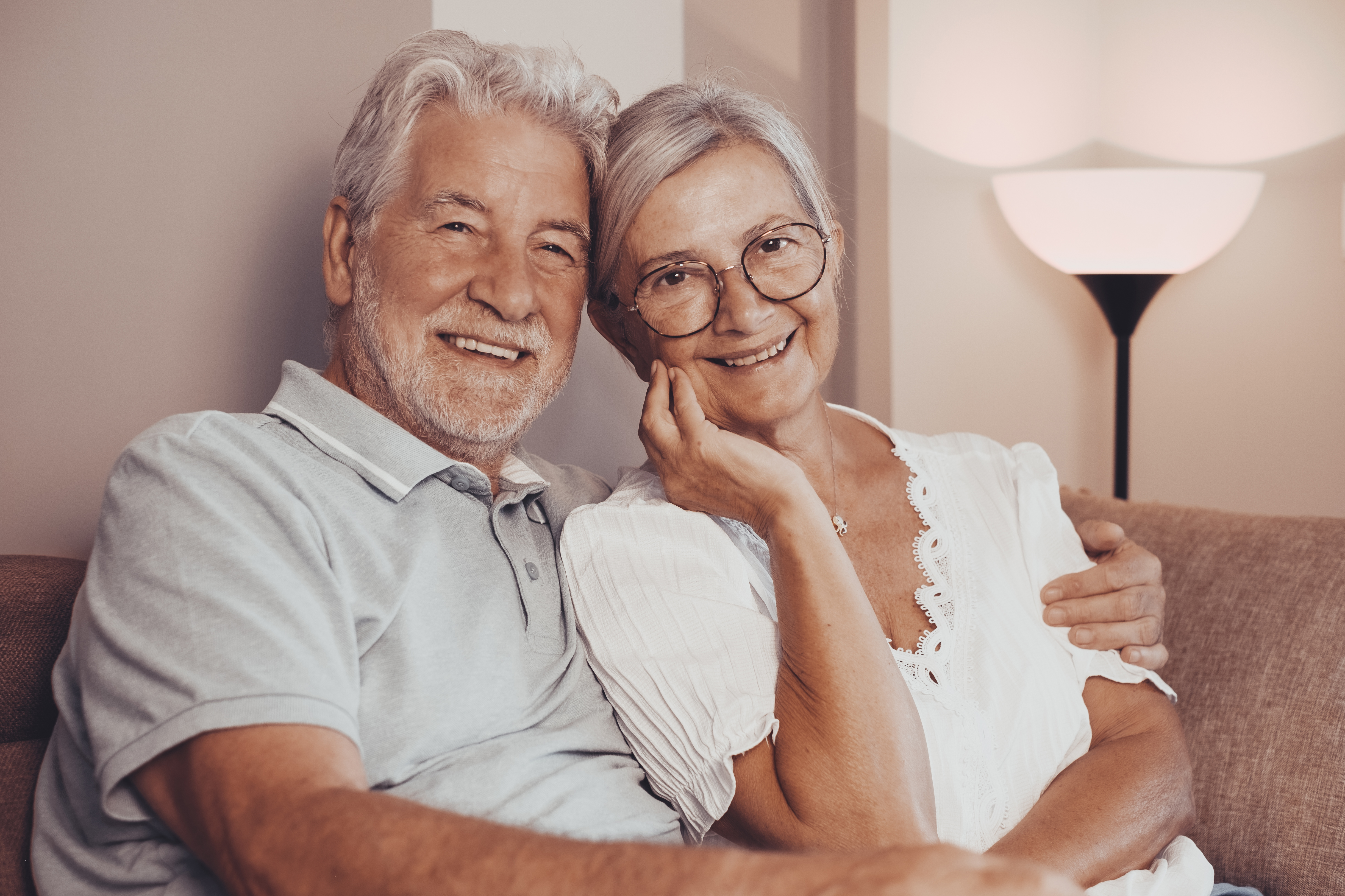 Happy bonding loving middle aged senior retired couple sitting on sofa, looking at camera