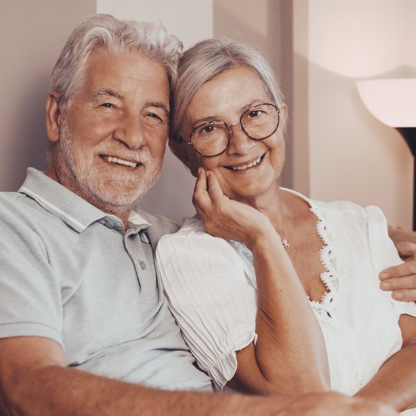 Happy bonding loving middle aged senior retired couple sitting on sofa, looking at camera